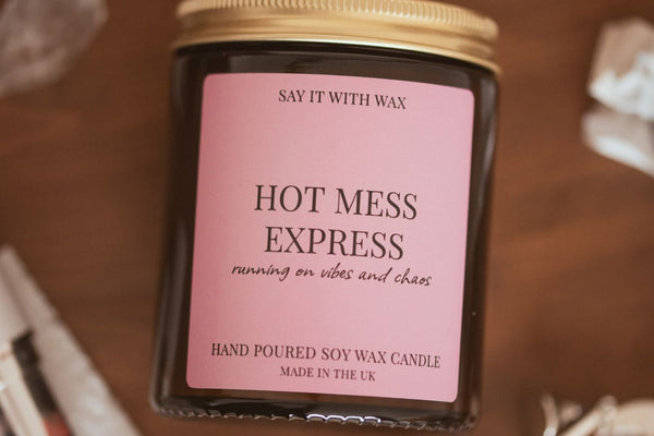 Overhead close-up of Hot Mess Express soy candle with lid on, wrapped gifts blurred in the background, for the Christmas Gifts for Women Who Have Everything blog post.
