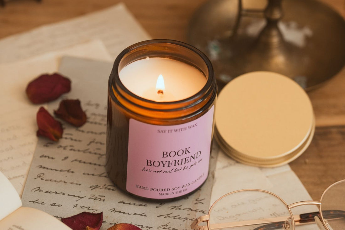 Lit Book Boyfriend soy candle beside handwritten letters, dried rose petals and reading glasses, for the Gifts for Your Bookish Best Friend blog post.