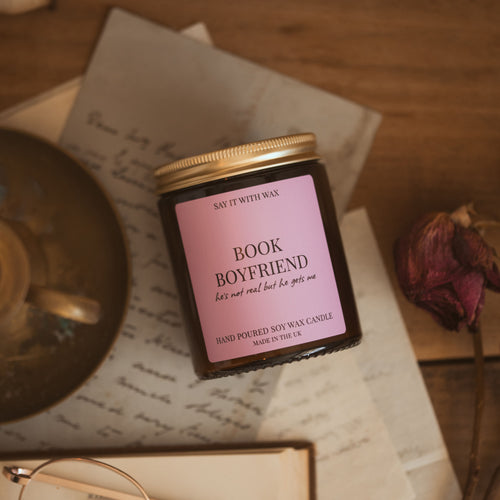 Book Boyfriend candle with gold lid on, resting on a handwritten letter beside a dried rose, hand-poured soy wax candle by Say It With Wax.