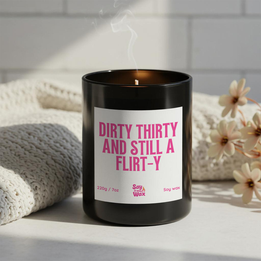Dirty Thirty and Still a Flirt-y soy wax candle in matte black glass jar with pink label and ash wooden lid, funny 30th birthday milestone gift