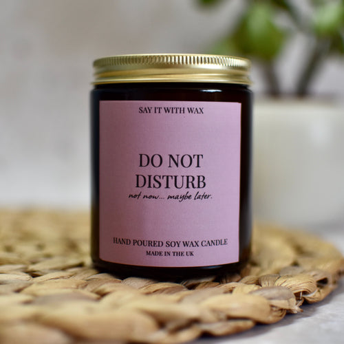 Do Not Disturb Candle with a purple label on a woven mat