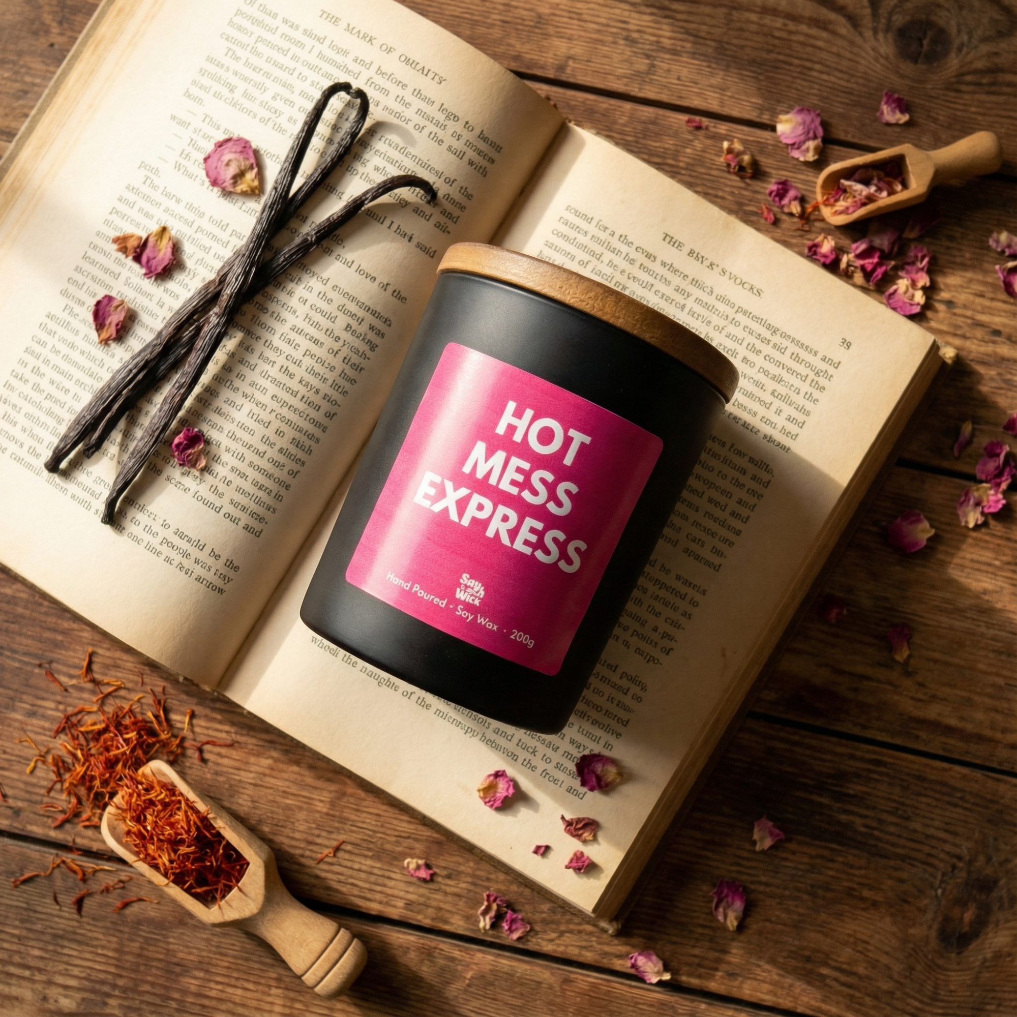 Candle labeled 'Hot Mess Express' on an open book with vanilla beans and dried flowers.
