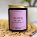 Candle with a pink label reading 'Reading Retreat' on a woven mat.