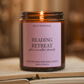 Say It With Wax Reading Retreat candle burning, pink label reading "plans cancelled, obviously", resting on an open book with a soft warm background.