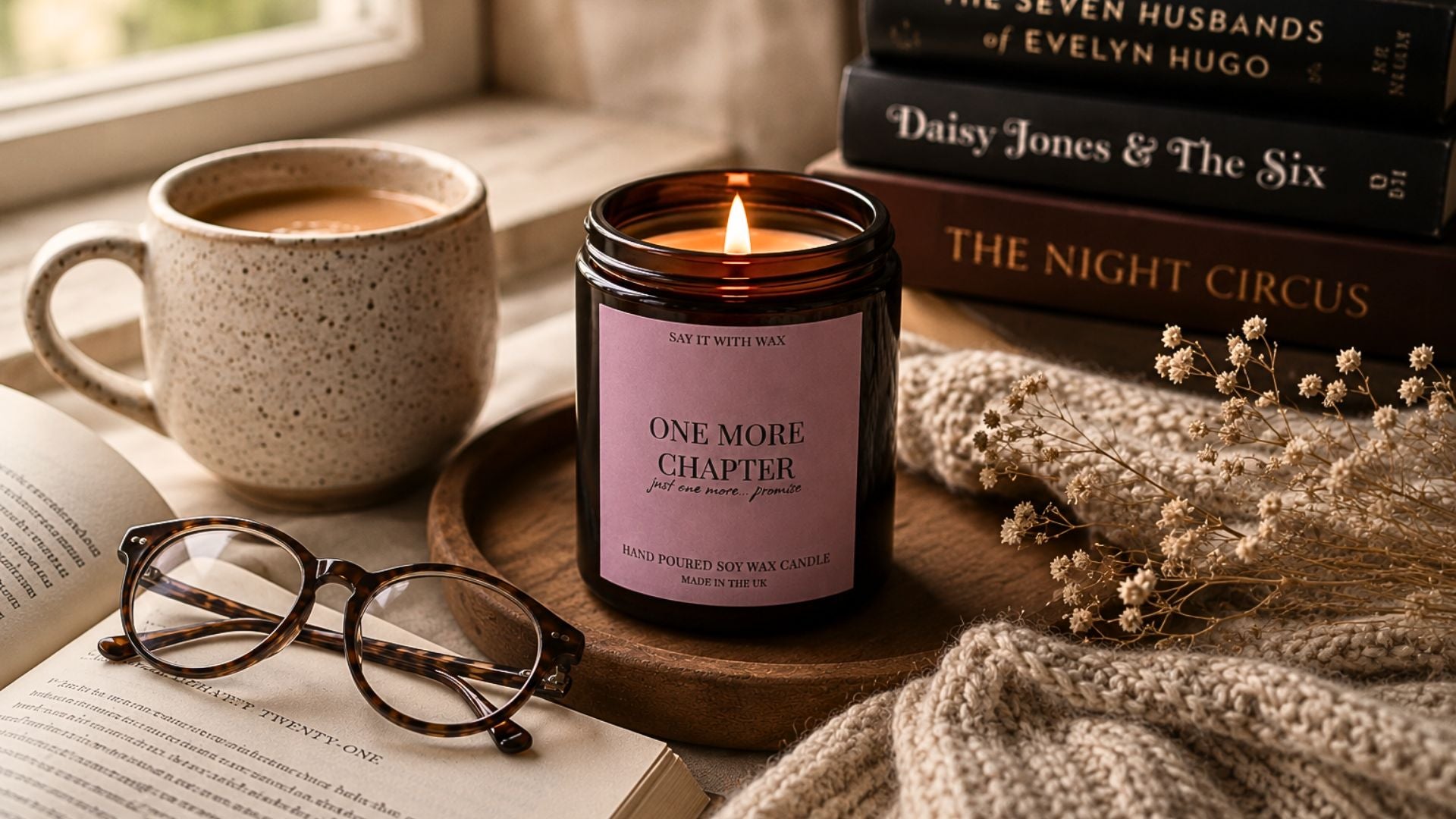 Candle labeled 'One More Chapter' with a mug, books, and glasses on a wooden surface.
