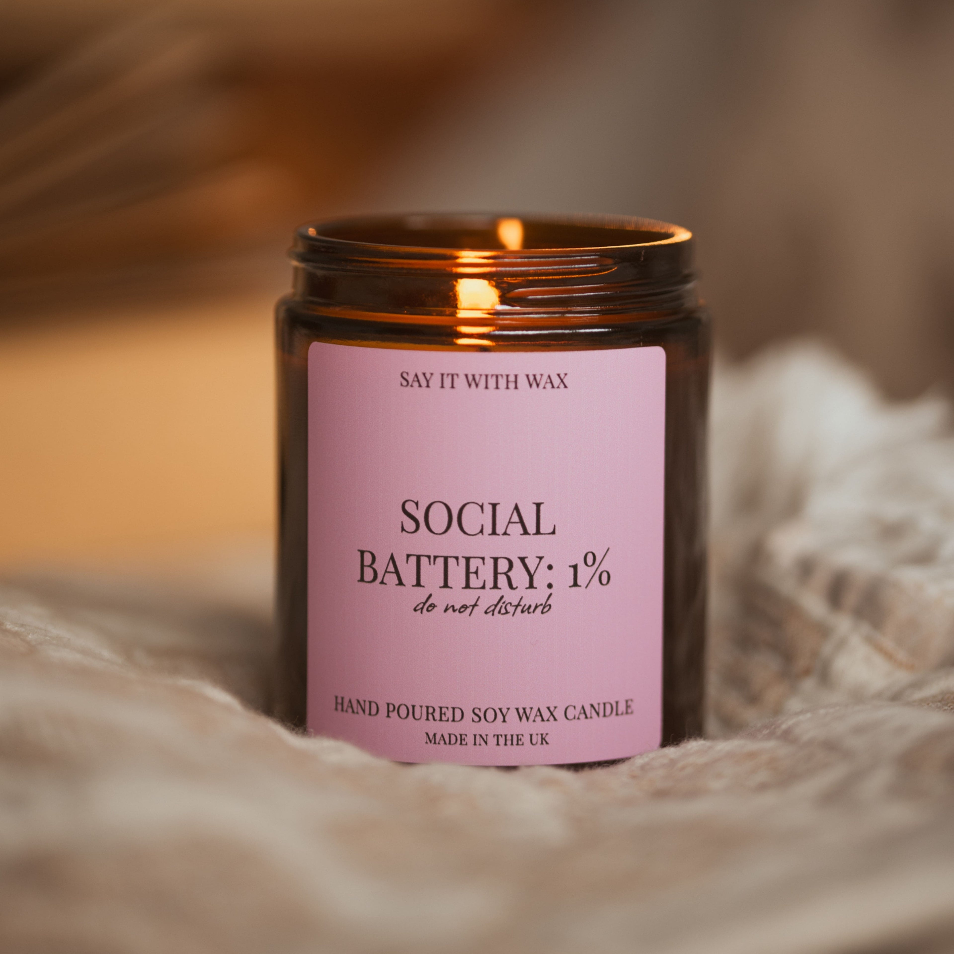 Lit Social Battery: 1% candle nestled in soft draped fabric, warm blurred background.
