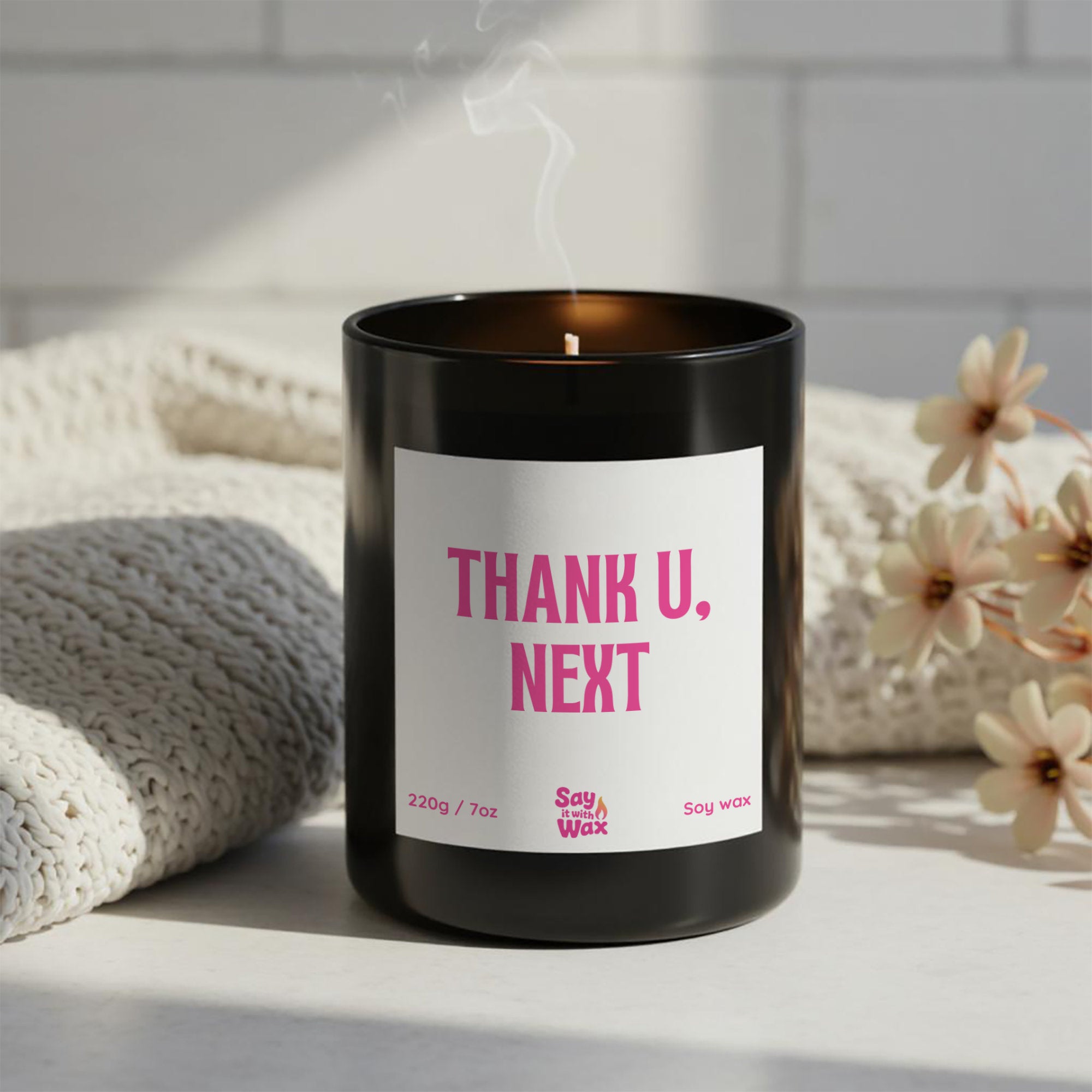 Thank U, Next” breakup candle in black glass vessel with pink label, soy wax, hand-poured by Say it With Wax, styled on white surface with flowers.