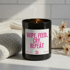Black candle with a pink label on a white surface with flowers and a towel in the background