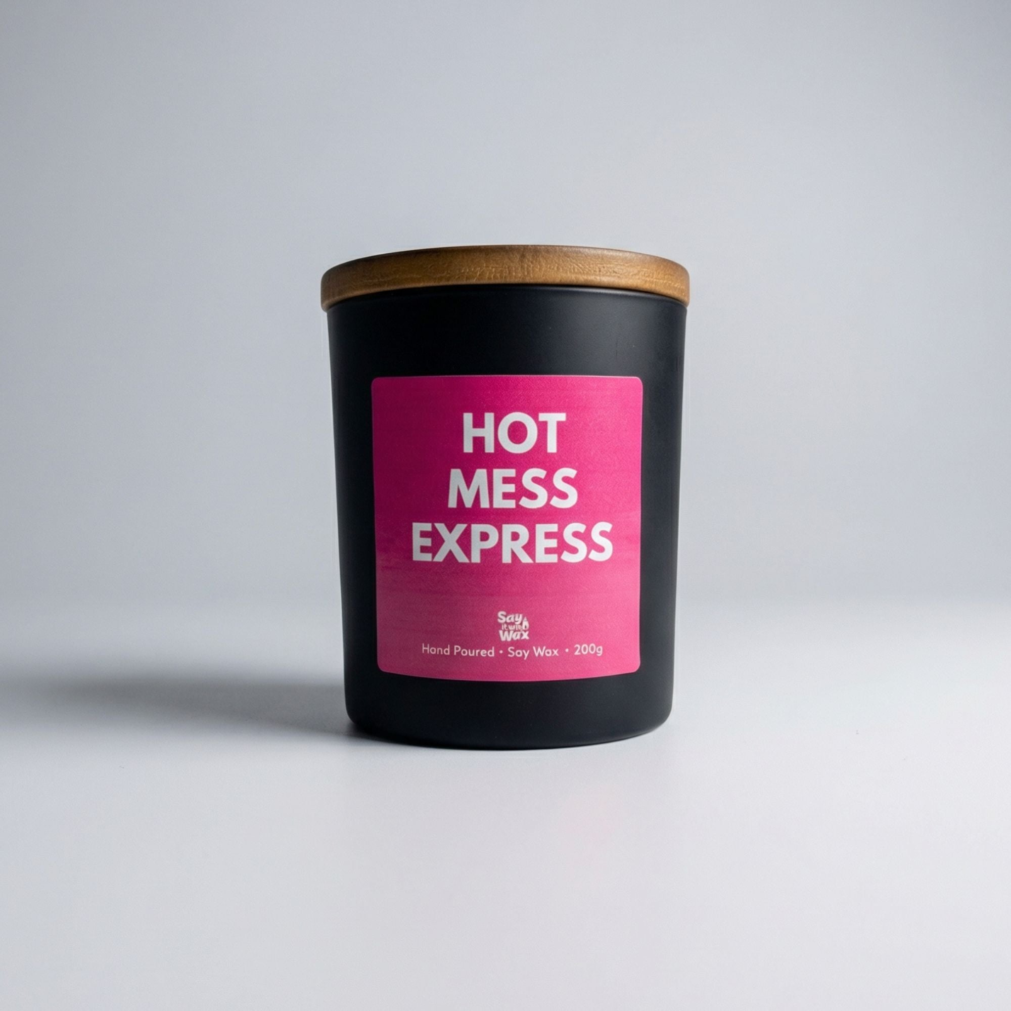 Black matte soy candle with a wooden lid and bright pink label reading “Hot Mess Express” by Say It With Wax, photographed on a clean white background. 