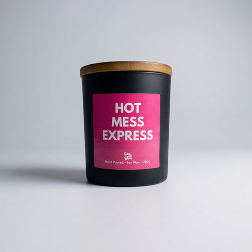 Black matte soy candle with a wooden lid and bright pink label reading “Hot Mess Express” by Say It With Wax, photographed on a clean white background. 