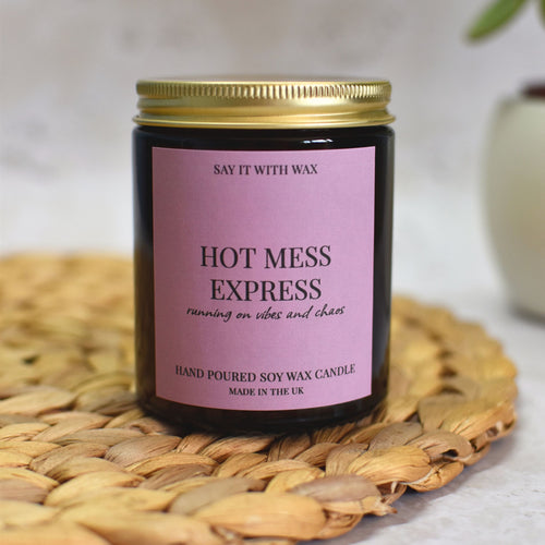 Hot Mess Express Soy Candle jar with pink label on a woven mat